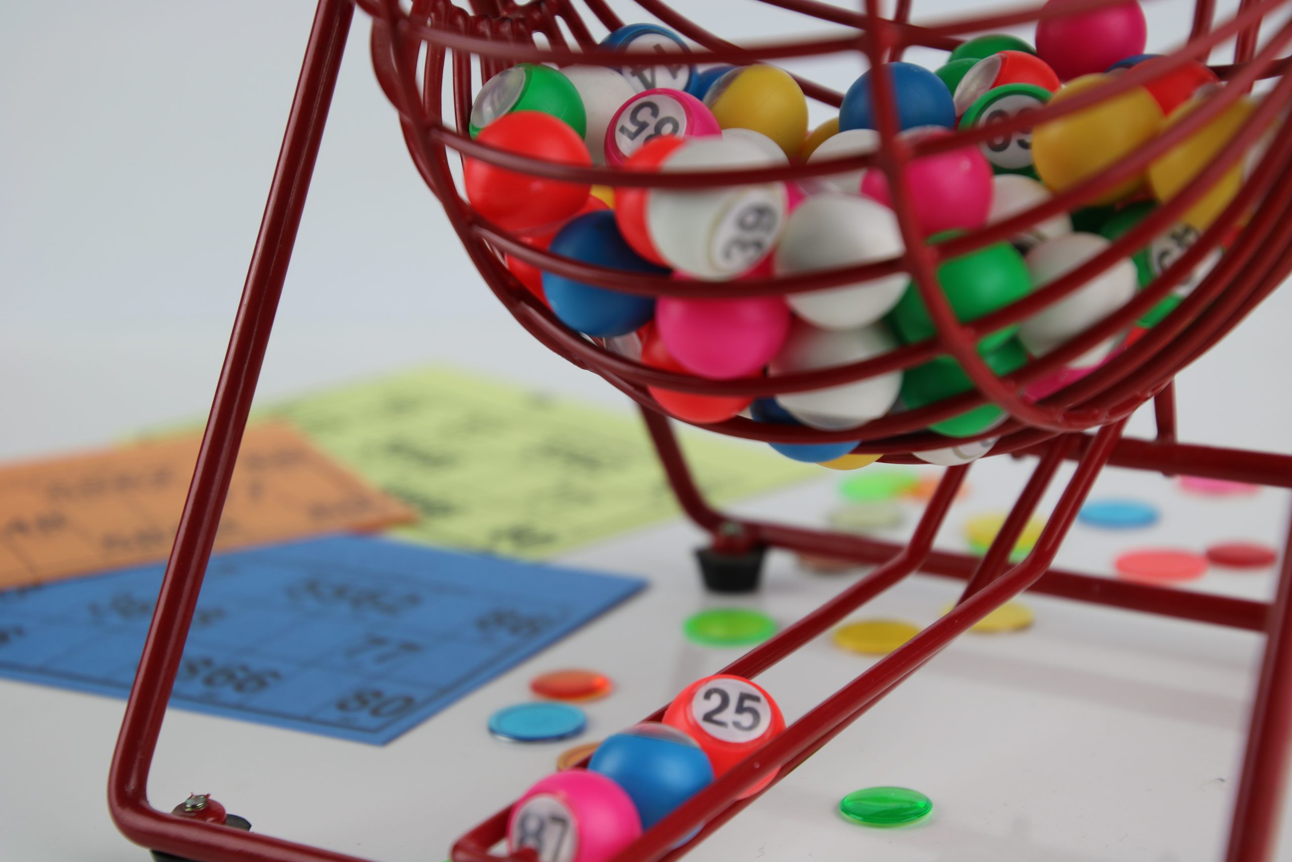 On imagine les boules tourner et le suspense du tirage qui augmente. Photo d'un boulier manuel de loto rouge, avec des boules de jeu colorées à l'intérieur et en fond des cartons de loto et des pions de marquage
